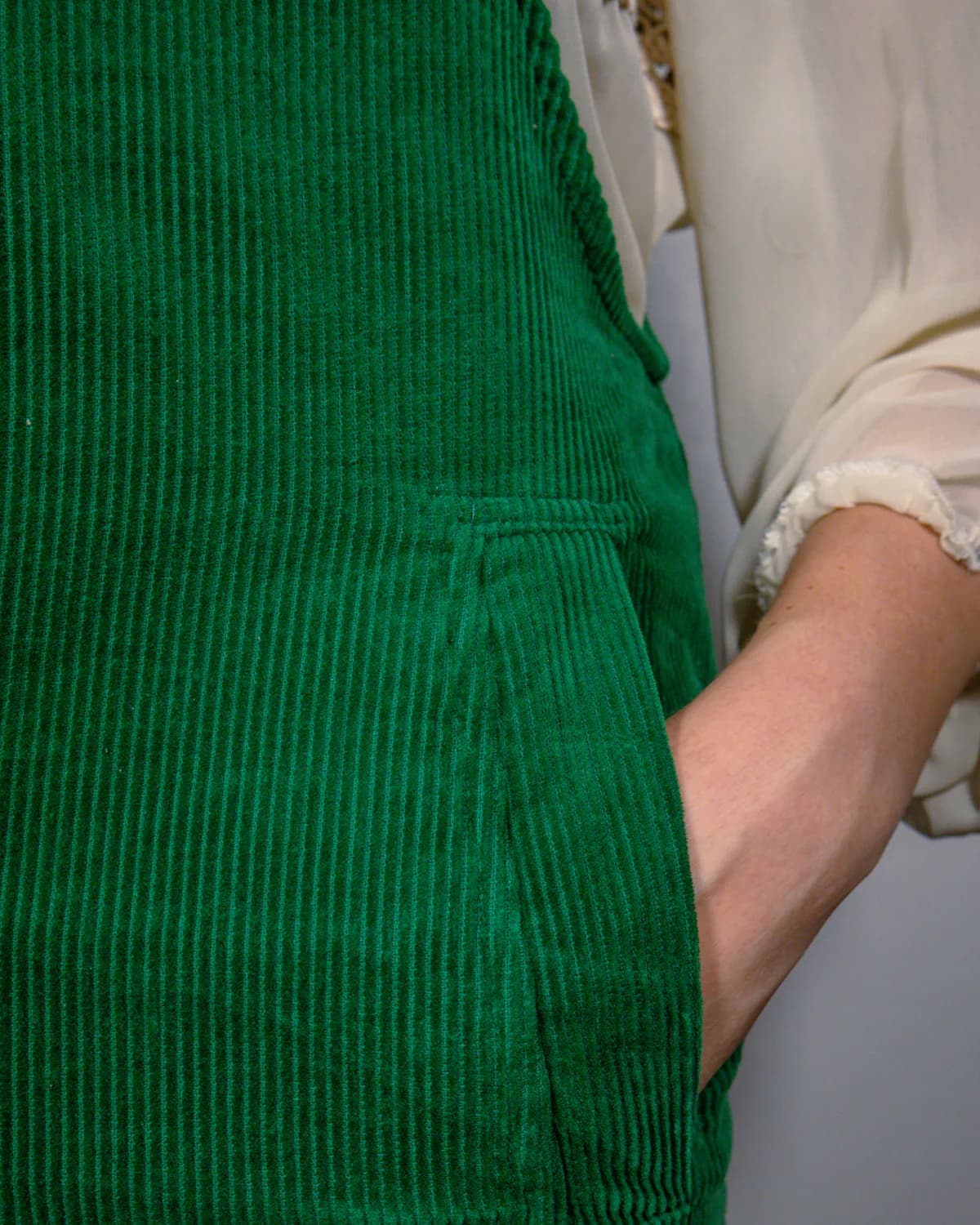 Close-up of forest green cotton corduroy with a side pocket and hand tucked inside, showing the ribbed texture.