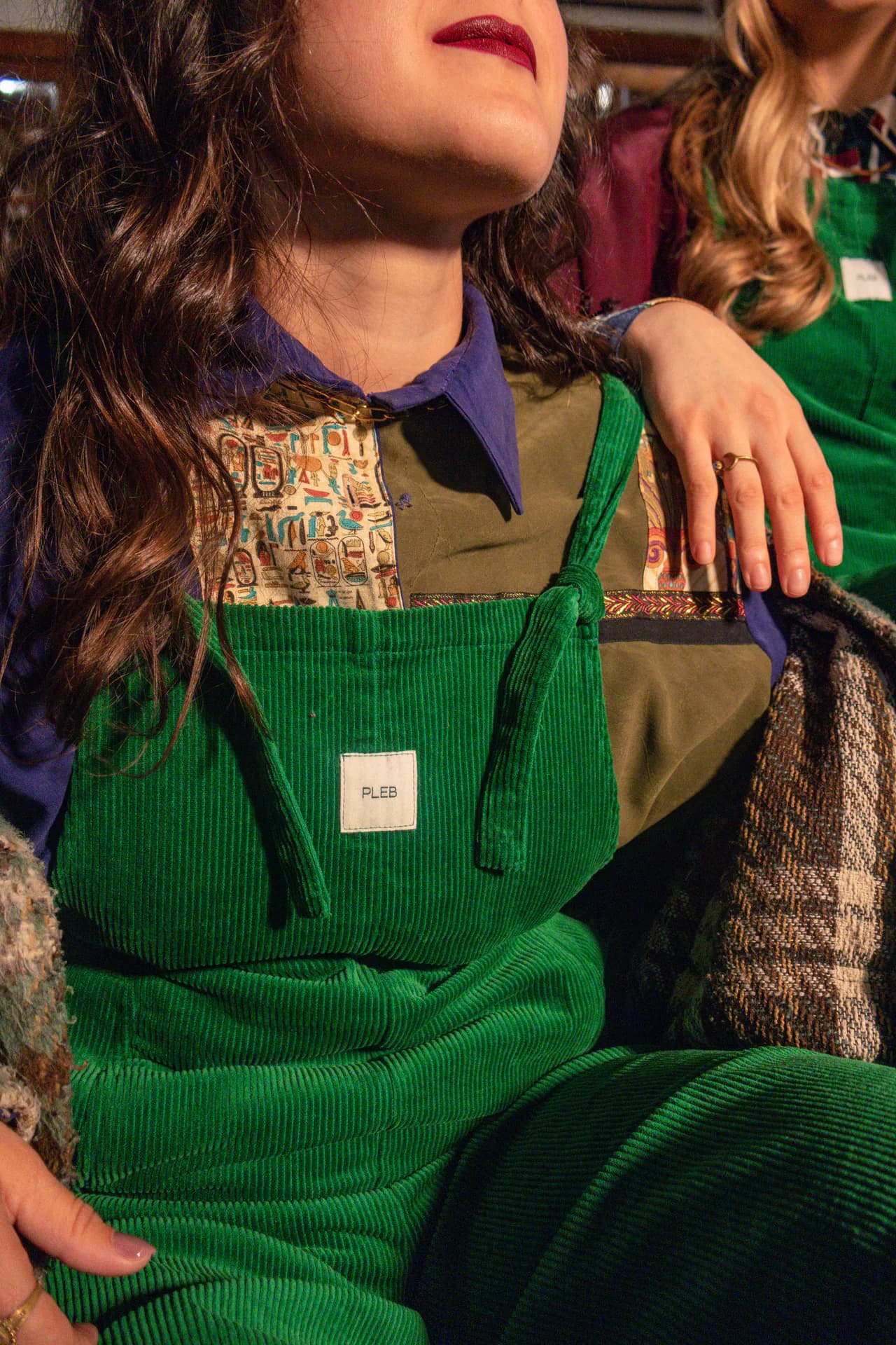 Close-up of forest green cotton corduroy dungarees showing the bib label and knotted self-fabric straps.
